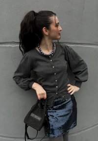 Γκρι ζακέτα με κουμπιά και φουσκωτά μανίκια, συνδυασμένη με μπλε φούστα με παγιέτες. Μαύρη τσάντα υφής με λευκό λογότυπο, αντίστοιχο κολιέ με χάντρες.