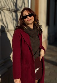 Βερντοπέ μάλλινο παλτό πάνω από καφέ πλεχτό ζιβάγκο, συνδυασμένο με μια λαμπερή βερντοπέ φούστα. Σκοτεινά γυαλιά ηλίου ολοκληρώνουν το σύνολο.