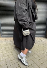 Svart oversized jakke over en svart topp, lagdelt med et svart skjørt. Sølvfargede sneakers med hvite sokker og en liten metallisk håndveske.