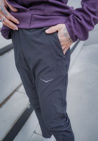 Svarta träningsbyxor med slät textur, utrustade med en sidoficka med dragkedja och en reflektiv logotypdetalj på låret.