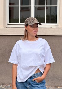 T-shirt bianca oversize, pantaloni shorts di denim e berretto da baseball con stampa leopardata. L'outfit presenta una vestibilità comoda e un design informale.