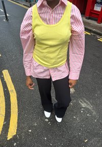 Maiou galben cu dungi, purtat peste un tricou cu mâneci lungi roz și alb cu dungi, asortat cu pantaloni negri cu picioare largi și pantofi albi.