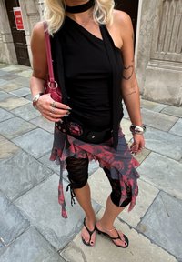 Black one-shoulder top, layered sheer floral skirt, black lace capri leggings, and black flip-flops. Silver ring accessories. Red handbag.