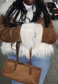 Bolso de ante marrón con detalles de cuero, combinado con una chaqueta de piel sintética cremosa y ante marrón. Vaqueros azules casuales completan el conjunto.