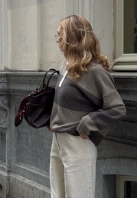 Sivi i smeđi prugasti oversized pulover s bijelim ovratnikom, uparen s krem hlačama širokih nogavica i tamnom torbom s maramom na točkice.