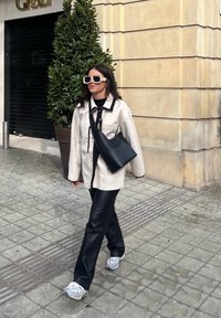 Υπερμεγέθης κρεμ ζακέτα με μαύρες λεπτομέρειες, μαύρο δερμάτινο παντελόνι, μαύρη τσάντα ώμου και λευκά γυαλιά ηλίου. Αθλητικά παπούτσια με γκρι λεπτομέρειες.