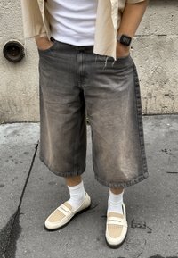 Tummanharmaat farkkukulotit väljällä istuvuudella, joissa on haalistunut pesu. Yhdistetty beigesävyisiin loafereihin ja valkoisiin sukkiin. Yksinkertainen yläosa ja rento tyyli.