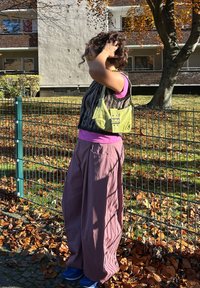 Sac à main vert avec détails de boucle, haut sans manches à imprimé animalier, sous-pull rose et pantalon large rose. Fond avec des feuilles d'automne.