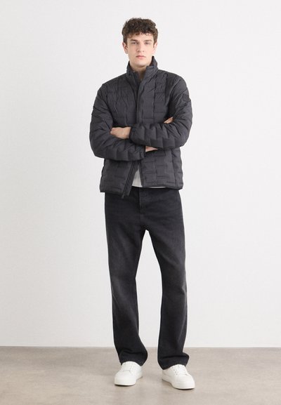 Chaqueta acolchada negra con textura geométrica, cuello alto y cierre de cremallera, combinada con pantalones de mezclilla oscuros y zapatillas blancas.