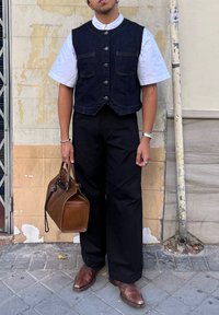 Denimvest over een wit T-shirt met korte mouwen, zwarte wijde broek, bruine leren handtas en bruine puntige laarzen. Zilveren sieraden accenten.