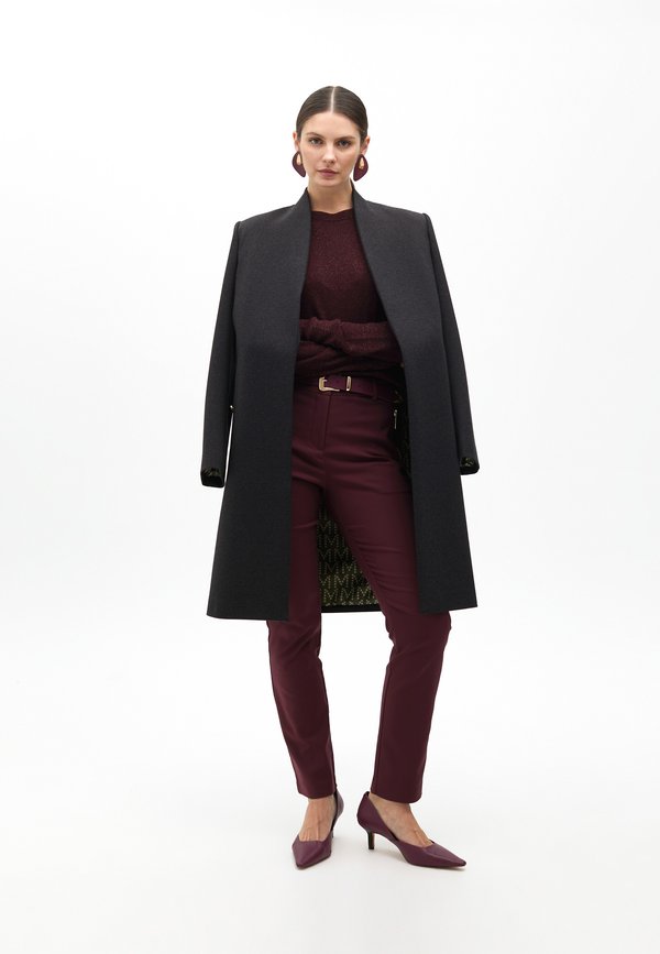 Cappotto lungo nero, maglione bordeaux, pantaloni bordeaux aderenti e tacchi a punta abbinati. Dettagli notevoli: maglione a trama, hardware dorato della cintura, interno patterned.