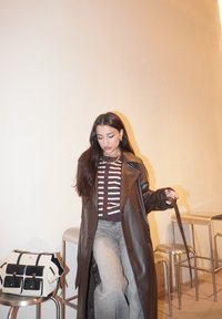 Barna bőr ballonkabát, csíkos bordó-fehér felső, világos farmernadrág, ezüst kiegészítők és egy krémszínű táska fekete díszítéssel.