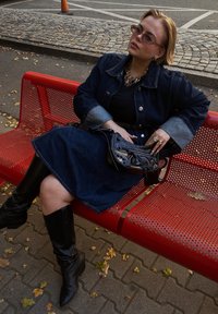 Τζάκετ τζιν με ανοιχτό μπλε μανίκια, μαύρη μπλούζα και σκούρα τζιν φούστα. Φορεμένο με μαύρες μπότες μέχρι το γόνατο και μικρή μαύρη τσάντα. Σε μια κόκκινη πάγκο.