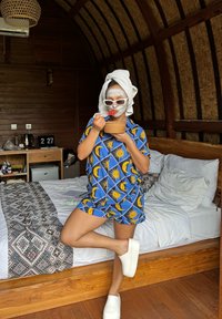 Blauwe pyjama set met een patroon van gele zonnen en halve manen, gecombineerd met witte instap schoenen. Persoon houdt een kom en een lepel vast.