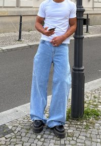 Jasnoniebieskie jeansy o szerokich nogawkach z lekko spranym wykończeniem, zestawione z czarnymi masywnymi butami i dopasowanym białym t-shirtem.