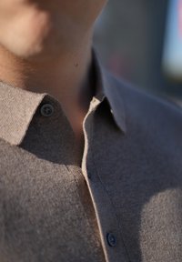 Brown button-up shirt made from textured fabric, featuring a classic collar and dark buttons, shown in close-up detail.