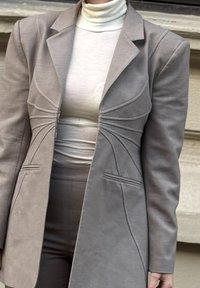 Hall hallikas struktureeritud bleiser tekstuurse kangaga, mis on varustatud lõigatud õmblustega, esitaskute ja erilise voltimisega vöökoha juures.