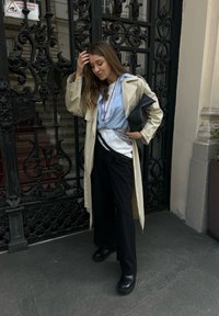 Bežna trench jakna, svetlo modra srajca, črne hlače, črna obutev, črtast šal. Dodatki vključujejo črno torbico in plastične verižice.