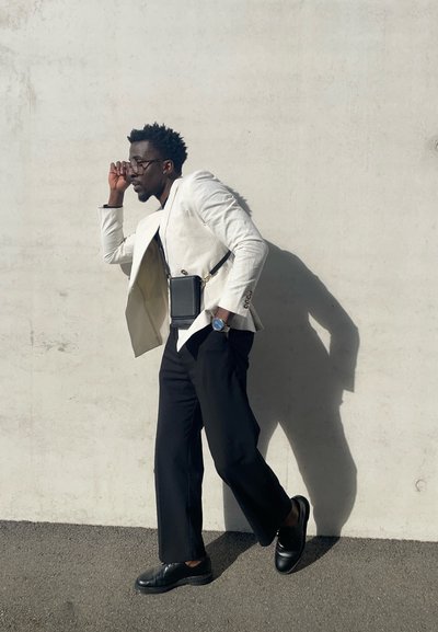 Blazer blanco de lino, pantalones anchos negros, bolso negro con correa, zapatos negros, accesorios con gafas y un reloj. Fondo neutro.