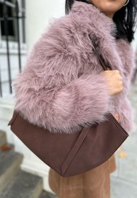 Flauschiger rosa Kunstpelzmantel kombiniert mit einer dunkelbraunen Leder-Umhängetasche, die eine glatte Textur und ein strukturiertes Design aufweist.