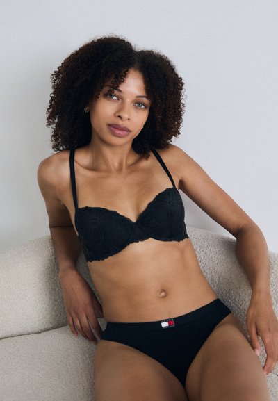 Sujetador de encaje negro con diseño acolchado y tirantes ajustables, combinado con braguitas de algodón negro que presentan un pequeño detalle del logo en la cintura.