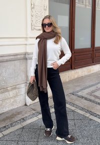 Hvid langærmet sweater, brun tørklæde, sort bredbenede jeans og mønstrede brune sneakers. Bærer en kviltet olivengrøn taske.
