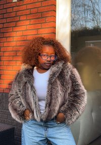 Veste en fausse fourrure grise à texture pelucheuse, coupe courte avec de larges revers, portée sur un haut blanc et associée à un jean bleu.