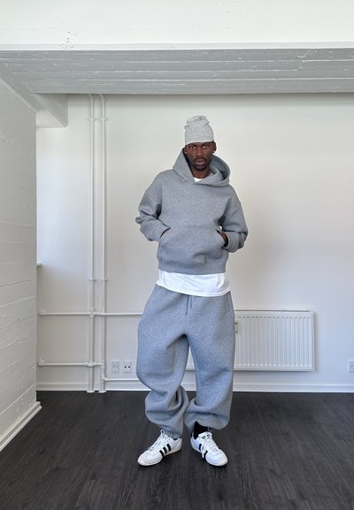 Sudadera gris y pantalones de chándal de mezcla de algodón, con un corte holgado. Los accesorios incluyen un gorro gris a juego y zapatillas blancas.
