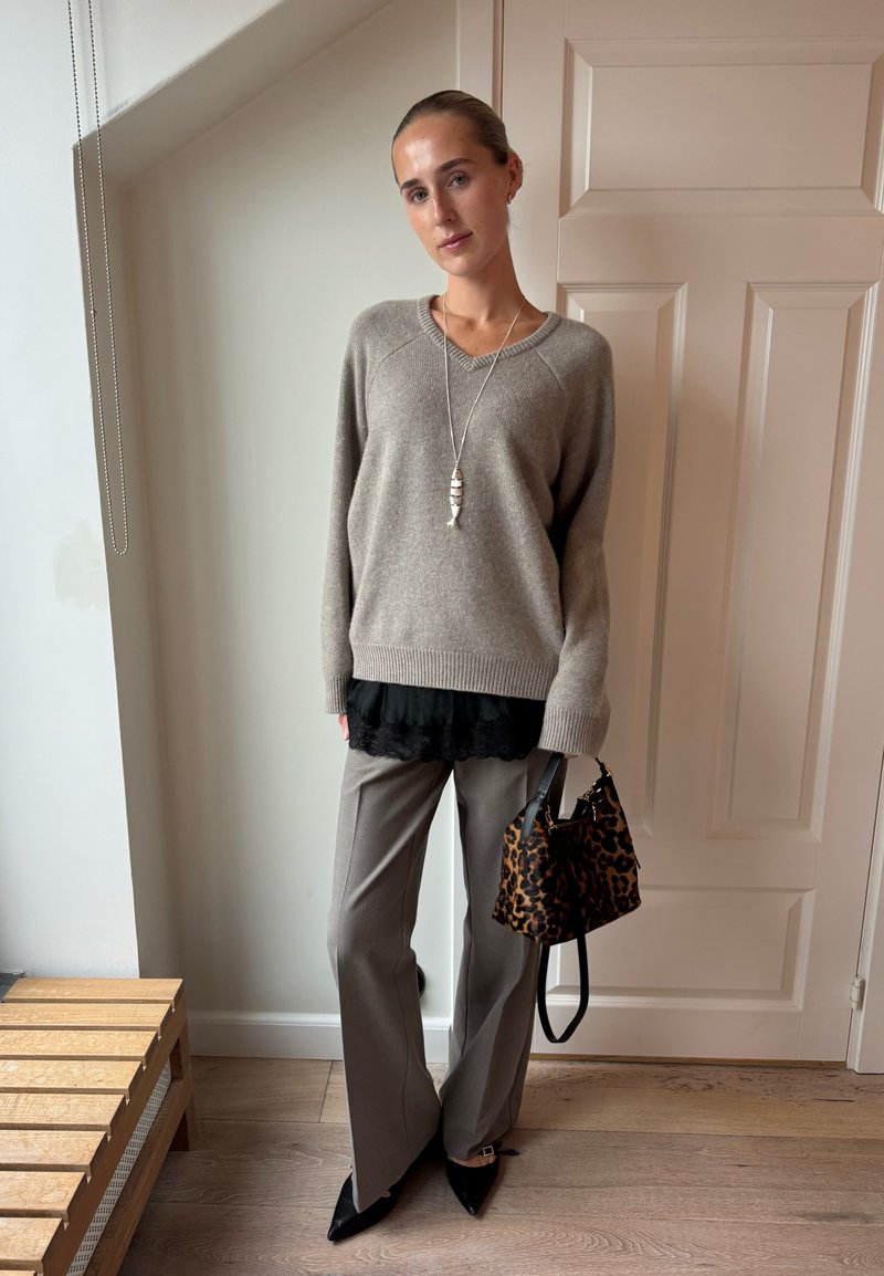 Bež pulover s V-izrezom, slojeviti crni čipkasti top, sivo široke hlače i torba s uzorkom leoparda. Izgled upotpunjuju crne špicaste štikle.
