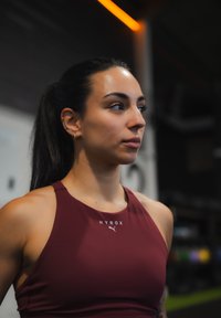 Mørkerød atletisk top med høj hals, med "HYROX" og Puma-logo. Glat tekstur, ærmeløs design, tætsiddende silhuet.