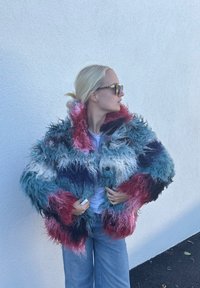 Kažokaina, daudzkrāsaina jaka zilās, rozā un baltās toņos ar pūkainu tekstūru un pārmērīgi lielu izmēru, papildināta ar lielām pogām.