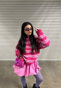 Sweater listrado rosa com pelugem, mangas longas, saia rosa rodada, collants lavanda e uma mini bolsa rosa brilhante. Óculos de sol roxos completam o look.