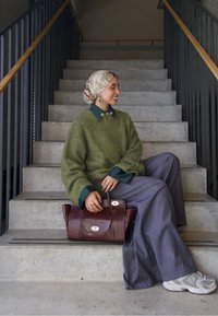 Zelený oversize svetr s modrým límečkem, šedé široké kalhoty, hnědá kabelka a bílé tenisky. V pozadí jsou betonové schody.