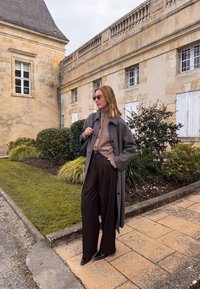 Lungo cappotto a motivo houndstooth, dolcevita beige, pantaloni larghi scuri e scarpe nere. Gli occhiali da sole e una borsa nera completano il look.