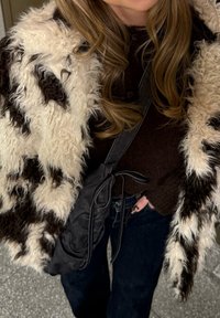 Teksturiran črno-beli krzneni plašč z dolgimi, grobimi vlakni; kombiniran s temnim puloverjem in črno torbo s podrobnostjo v obliki vozla.