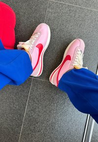Nike tenisky s růžovo-červenou barevnou kombinací, z materiálů semiš a kůže, s bílými tkaničkami a texturovanou gumovou podrážkou.