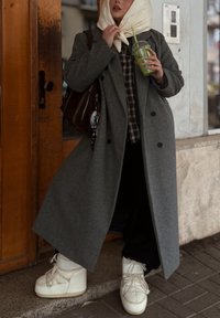 Szürke gyapjúkeverék kabát, bővebb szabású, kétsoros gombolású, kockás inggel párosítva. Fehér masszív platform cipő és barna táska.