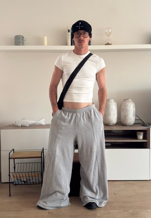 Pantalones sudadera grises claros con un corte holgado y bolsillos laterales, combinados con una camiseta blanca ajustada y una boina negra, de pie en el interior.