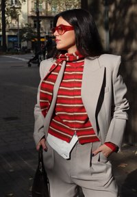 Lichtgrijs op maat gemaakt pak met oversized revers, rode en crèmekleurige gestreepte trui, rode sjaal, rode zonnebril en witte schoudertas.