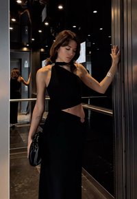 Melns halter top ar asimetrisku dizainu, kopā ar melnu svārku. Spīdīga tekstūra, minimālas sudraba detaļas un maza melna rokassoma.