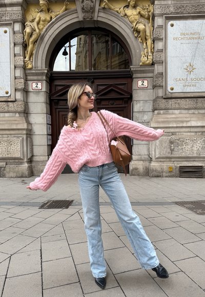 Suéter de punto en color rosa con un escote ancho, combinado con jeans de campana en azul claro y tacones negros de punta. Bolsa marrón con un acento rosa.
