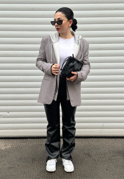 Blazer gris claro sobre una sudadera gris, combinado con pantalones de imitación cuero negros y zapatillas blancas. El accesorio incluye un bolso pequeño negro.