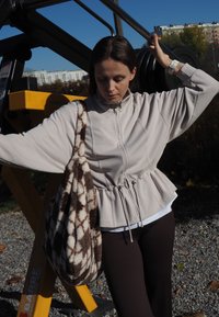 Lichtbeige zip-up jas met een drawstring taille, brede mouwen, gecombineerd met een gestructureerde tas in bruin en wit met patroon en bruine legging.