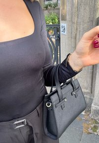 Borsa mini nera realizzata in materiale testurizzato con accenti dorati. Presenta due manici corti e una forma strutturata. Indossata insieme a una maglietta nera.