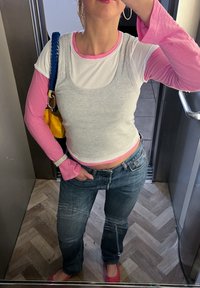 Femme portant des hauts superposés rose et blanc, un jean bleu, des chaussures roses, et portant un sac jaune avec une sangle bleue, debout dans un ascenseur.