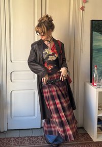 Καφέ δερμάτινο παλτό πάνω από ένα  floral τοπ, καρό μακρύ φούστα με μαύρη καρό ζώνη, πολλαπλά επίπεδα τζη�ν και διακριτικά αξεσουάρ κοσμημάτων.