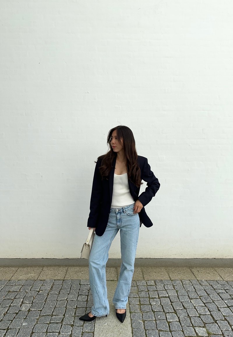 Μαύρο σακάκι πάνω από λευκή μπλούζα, ανοιχτό μπλε τζιν και μυτερές μαύρες γόβες. Μια μικρή κρέμα τσάντα ολοκληρώνει το σύνολο.