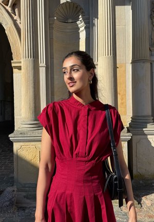 Vestido rojo de manga abullonada con cintura ajustada y falda plisada, combinado con un pequeño bolso cruzado negro y pendientes de aro dorados.