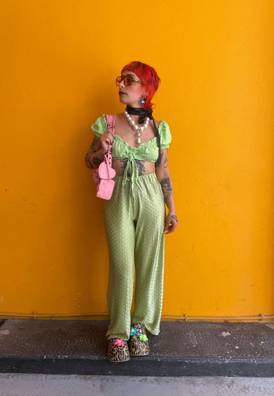 Top corto verde texturizado con mangas abullonadas; pantalones de pierna ancha a juego. Bolso rosa, zuecos de estampado de leopardo gruesos y collar de perlas en capas.