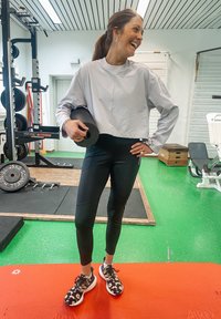 Mustat legginsit, vaaleanharmaa lyhythihainen collegepusero ja musta-valkoiset leopardikuosiset lenkkarit. Pitelee mustaa painoa kuntosalilla.
